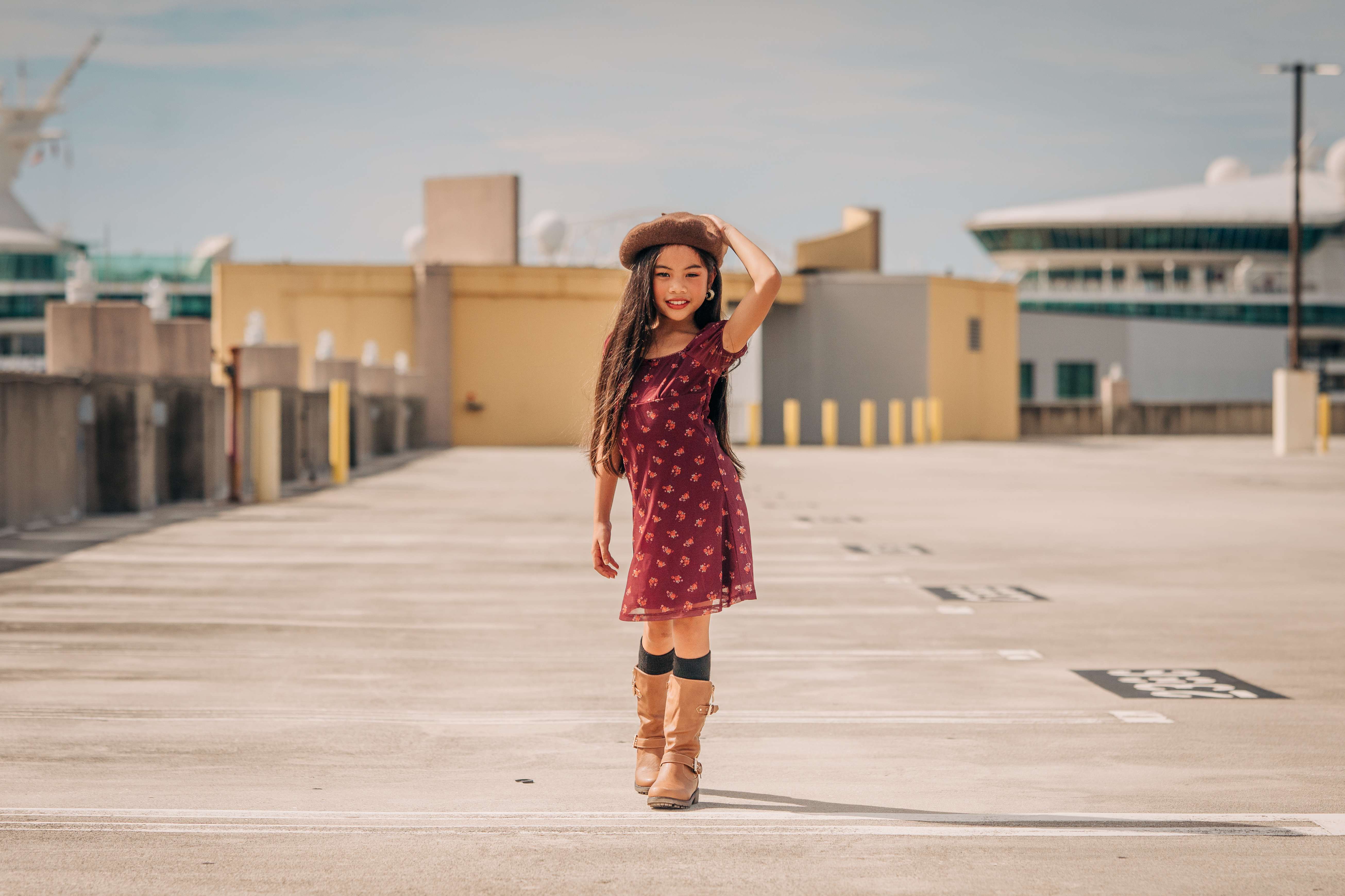 Pichara Luong in a burgundy floral dress, brown beret, and tan knee-high boots on a sunny rooftop